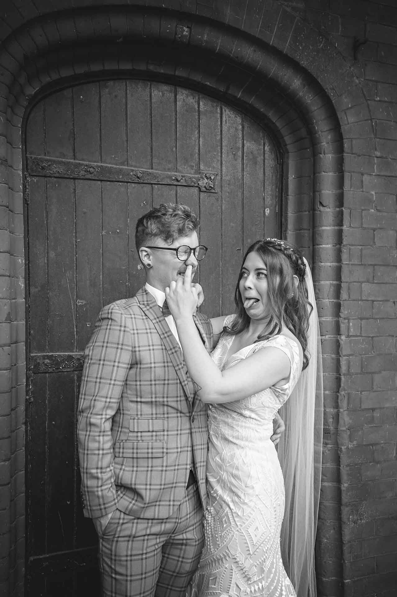 Bride sticking finger up groom's nose and sticking out tongue