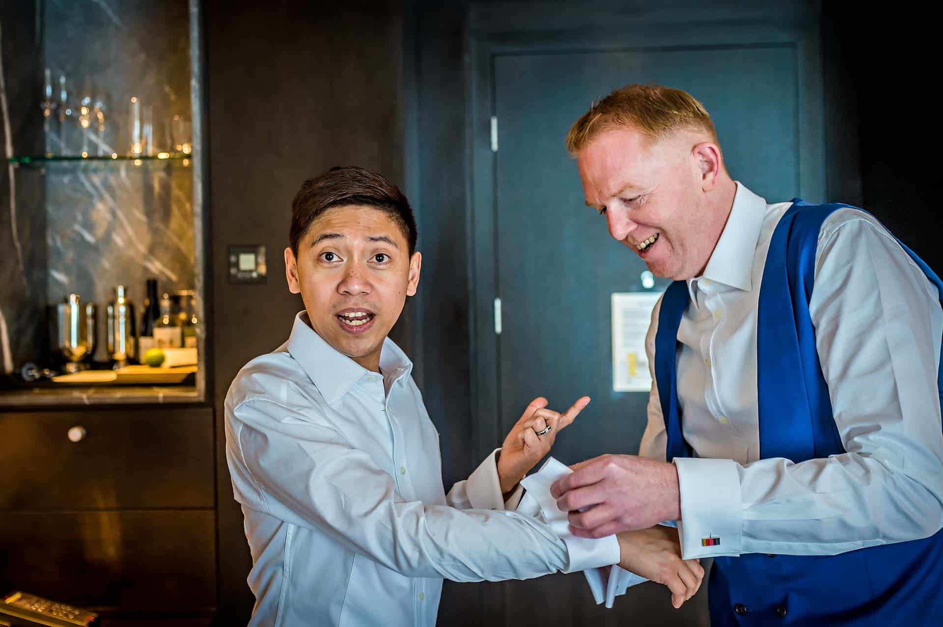 Groom pointing at groom whilst having his cuffs buttoned at gay wedding preparations