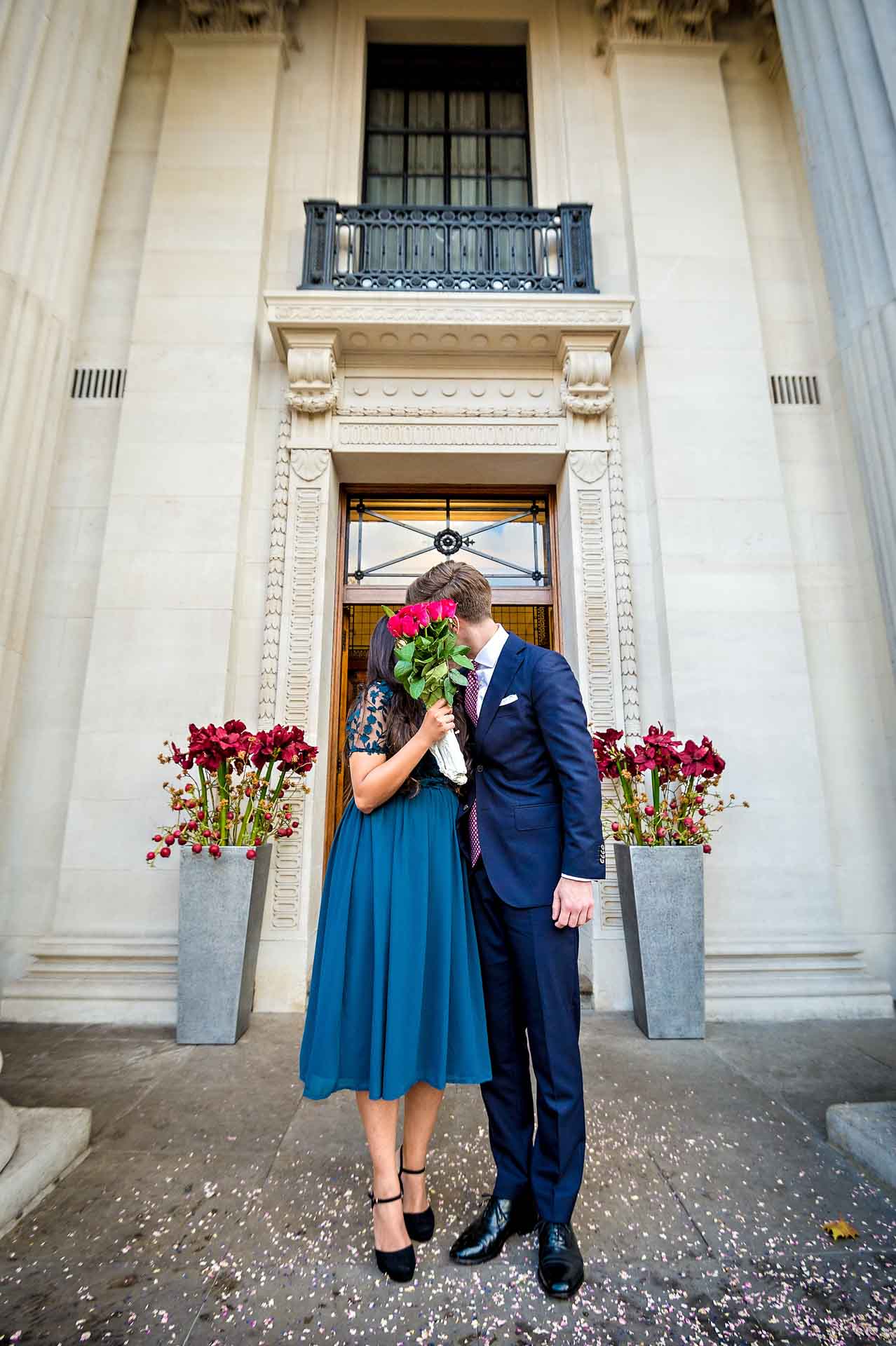 Bride hiding face with flowers whilst kissing groom outside Old Marylebone Town Hall