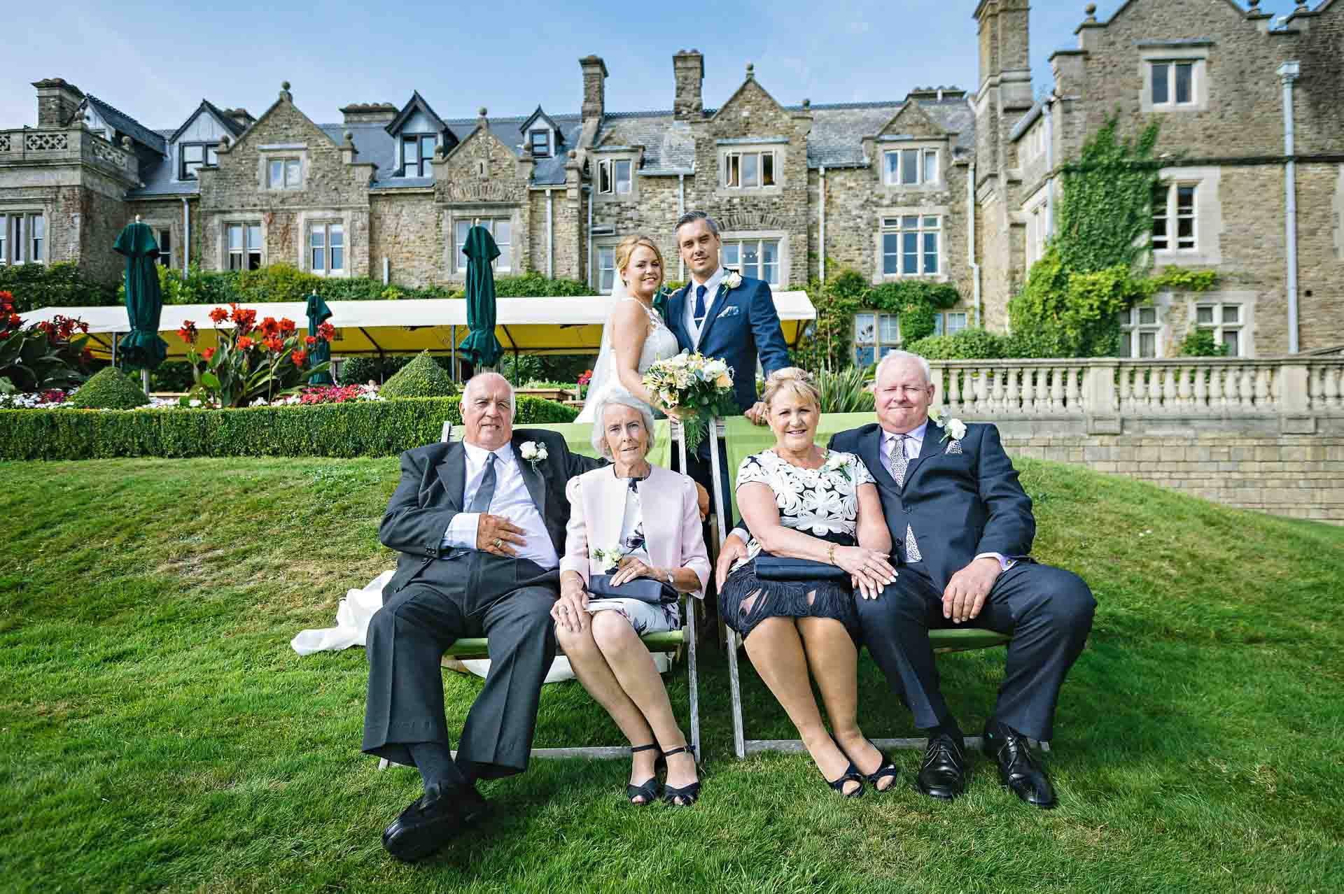 Four old people sitting in deck chairs with bride and groom in background at South Lodge Hotel, Horsham