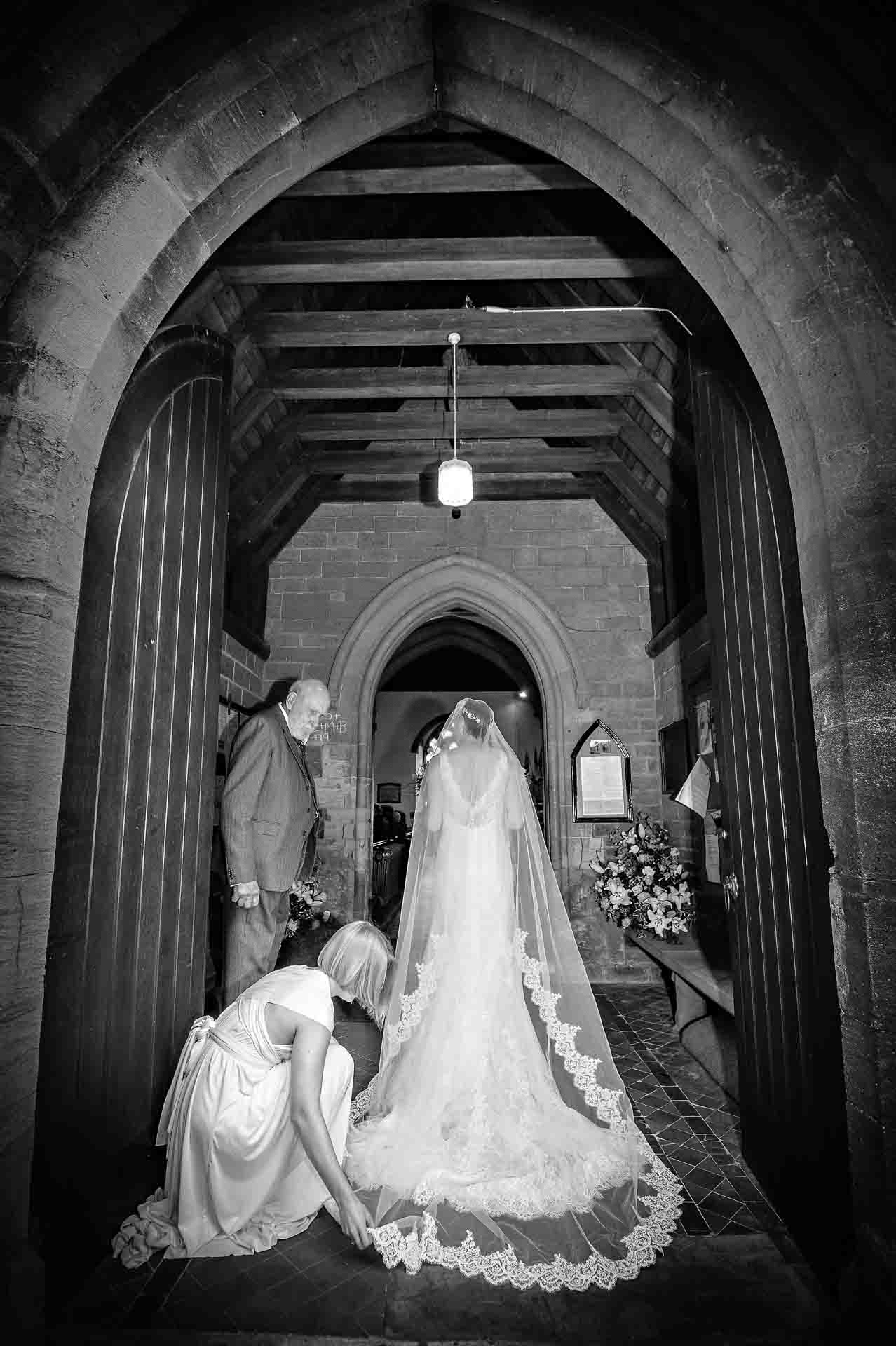 Bridesmaid arranging bride's dress in church doorway