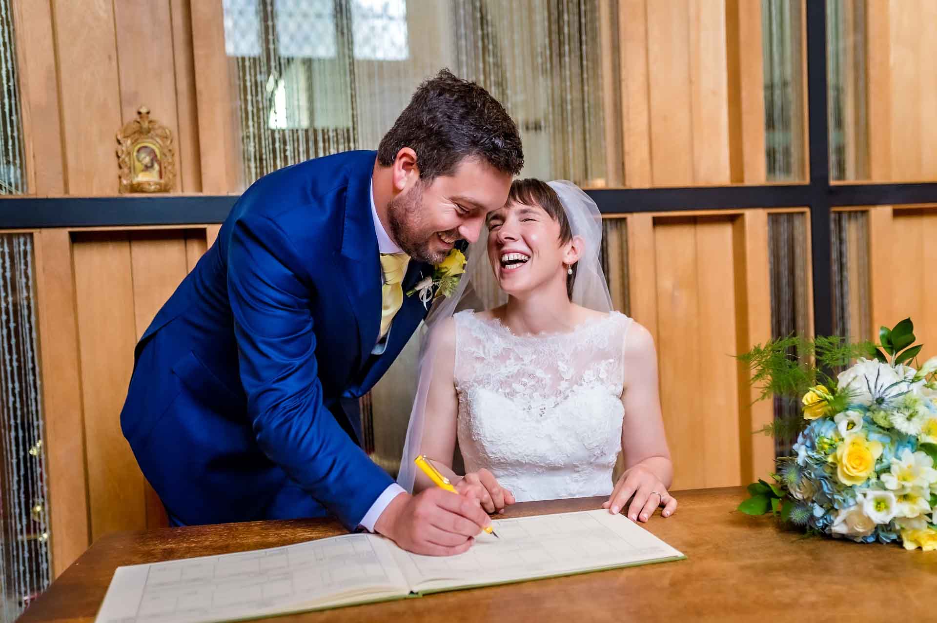 Bride laughing as groom pretends to sign the register at church wedding