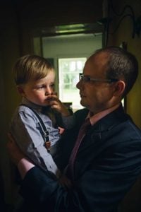 Boy toddler looking worried and being held by father at wedding