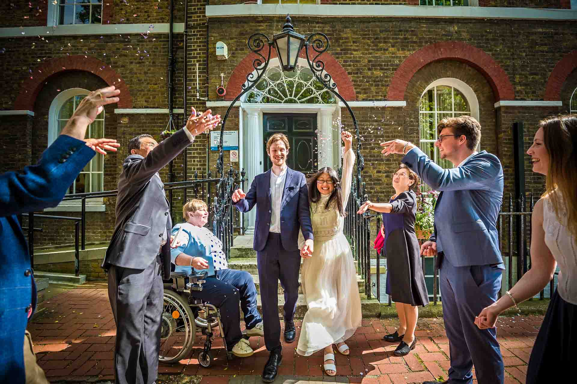 Guests throw confetti over couple whilst bride punches the air at Southwark Register Office