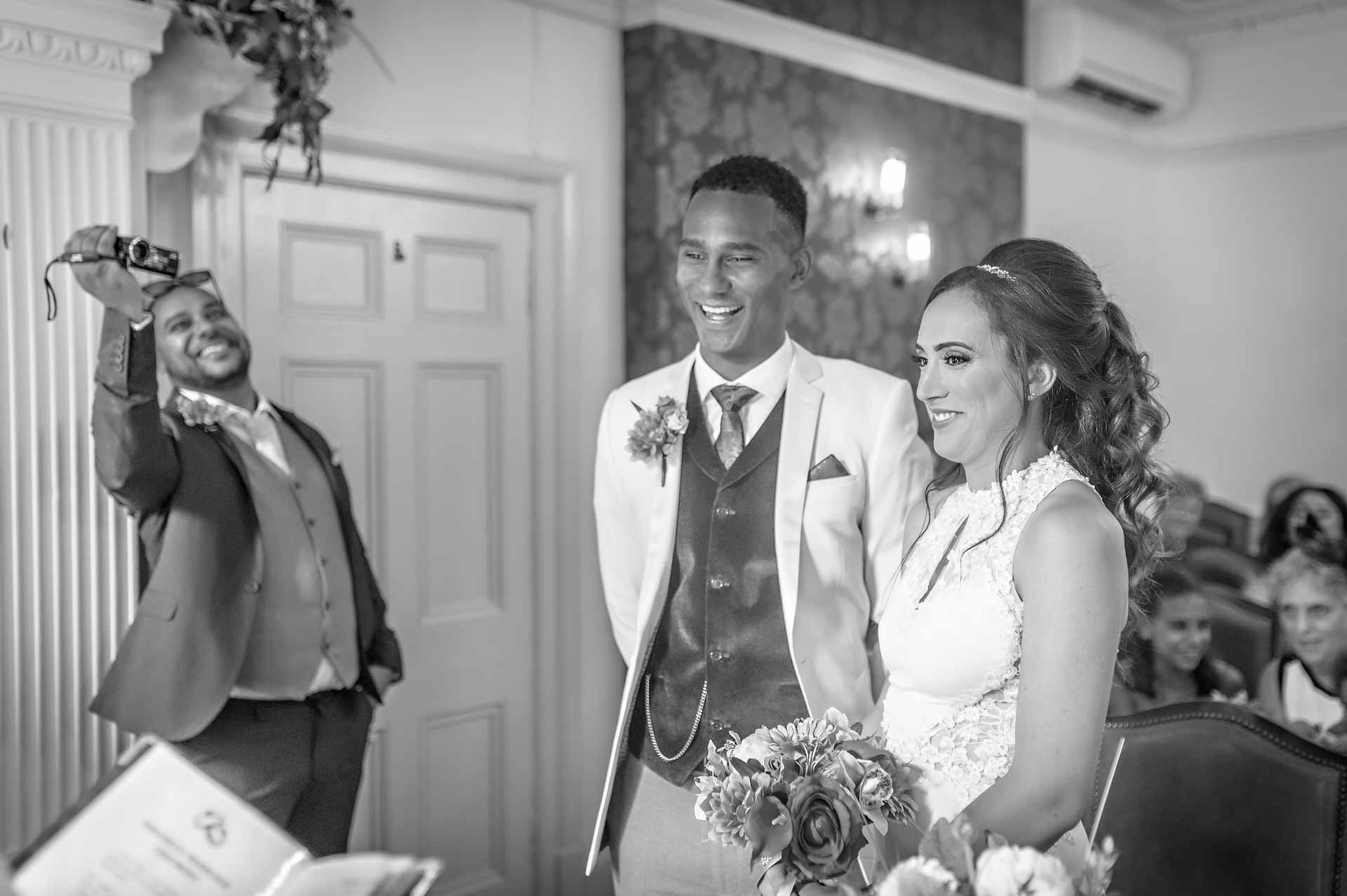 Bride and groom at register office wedding laughing whilst being videoed