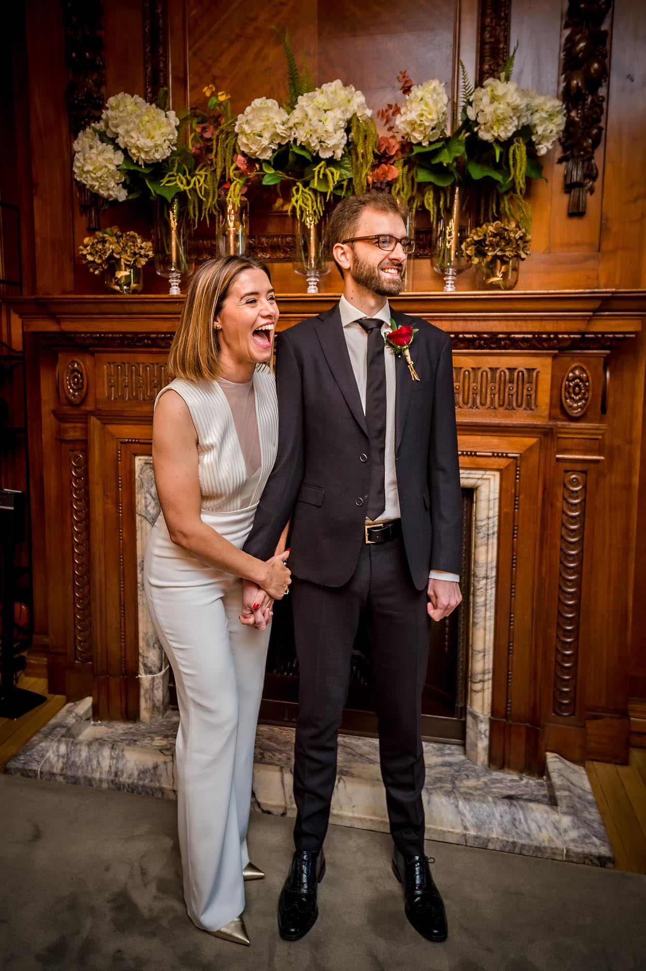Bride laughing out loud with groom in front of wooden fireplace at Old Marylebone Town Hall