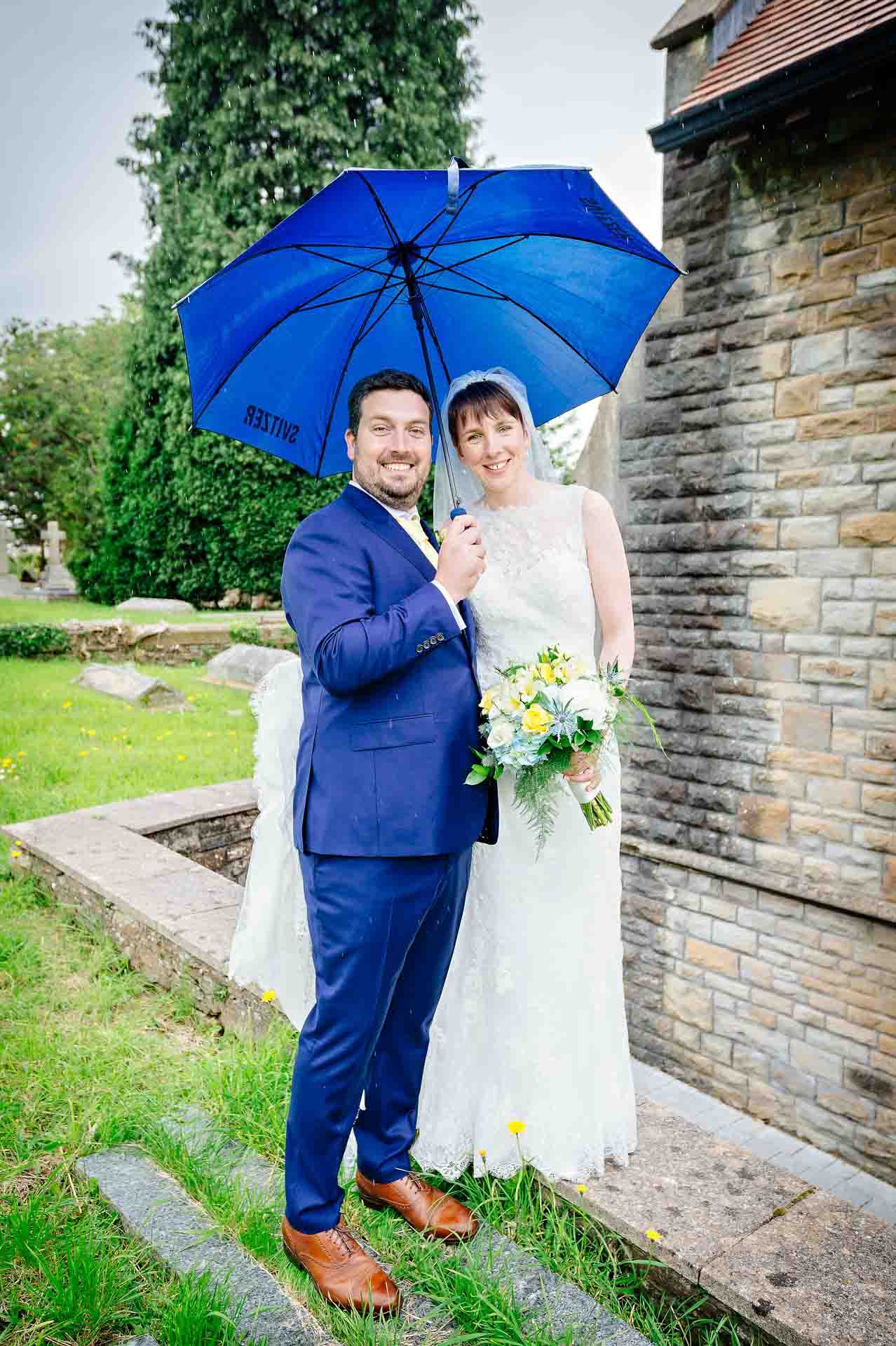 Happy couple with an umbrella smiling at camera outside church