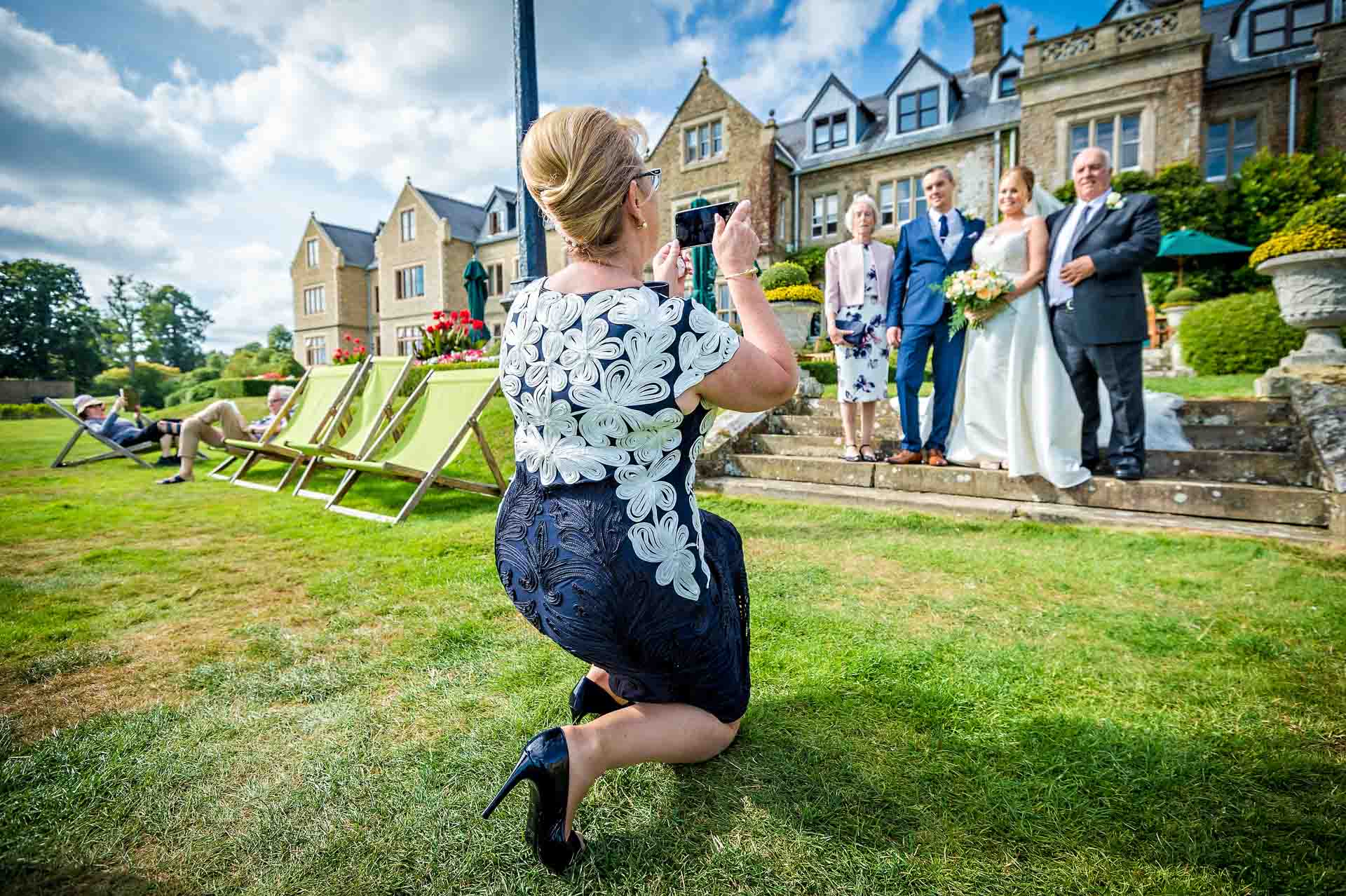 Lady at wedding crouching down taking a group photo on steps of South Lodge, Horsham