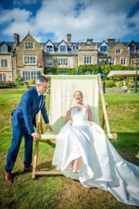 Bride laughing whilst getting into oversized armchair with groom leaning on it