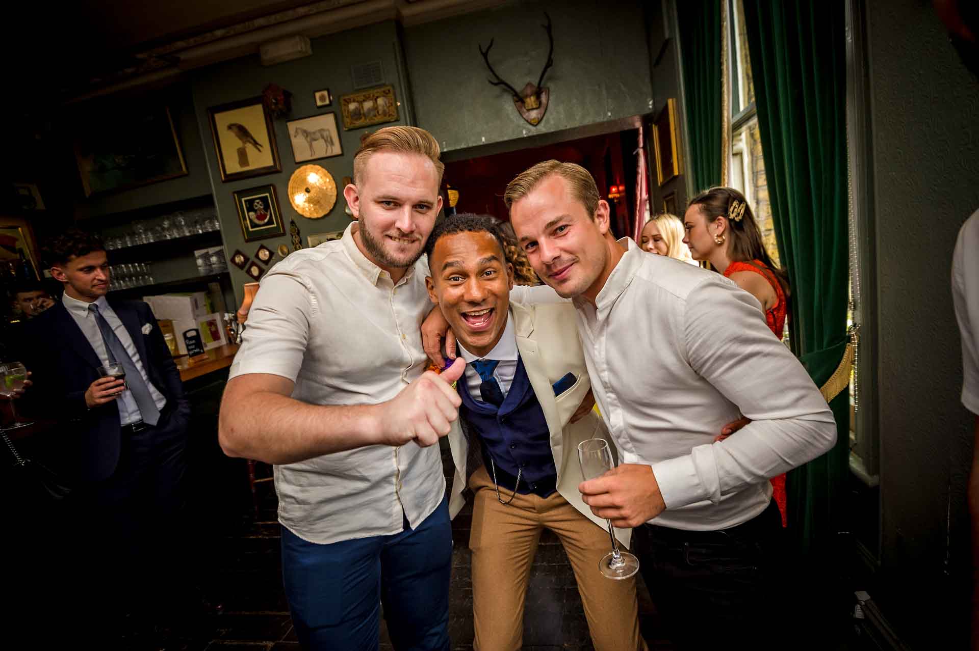 Groom between two friends smiling at wedding reception