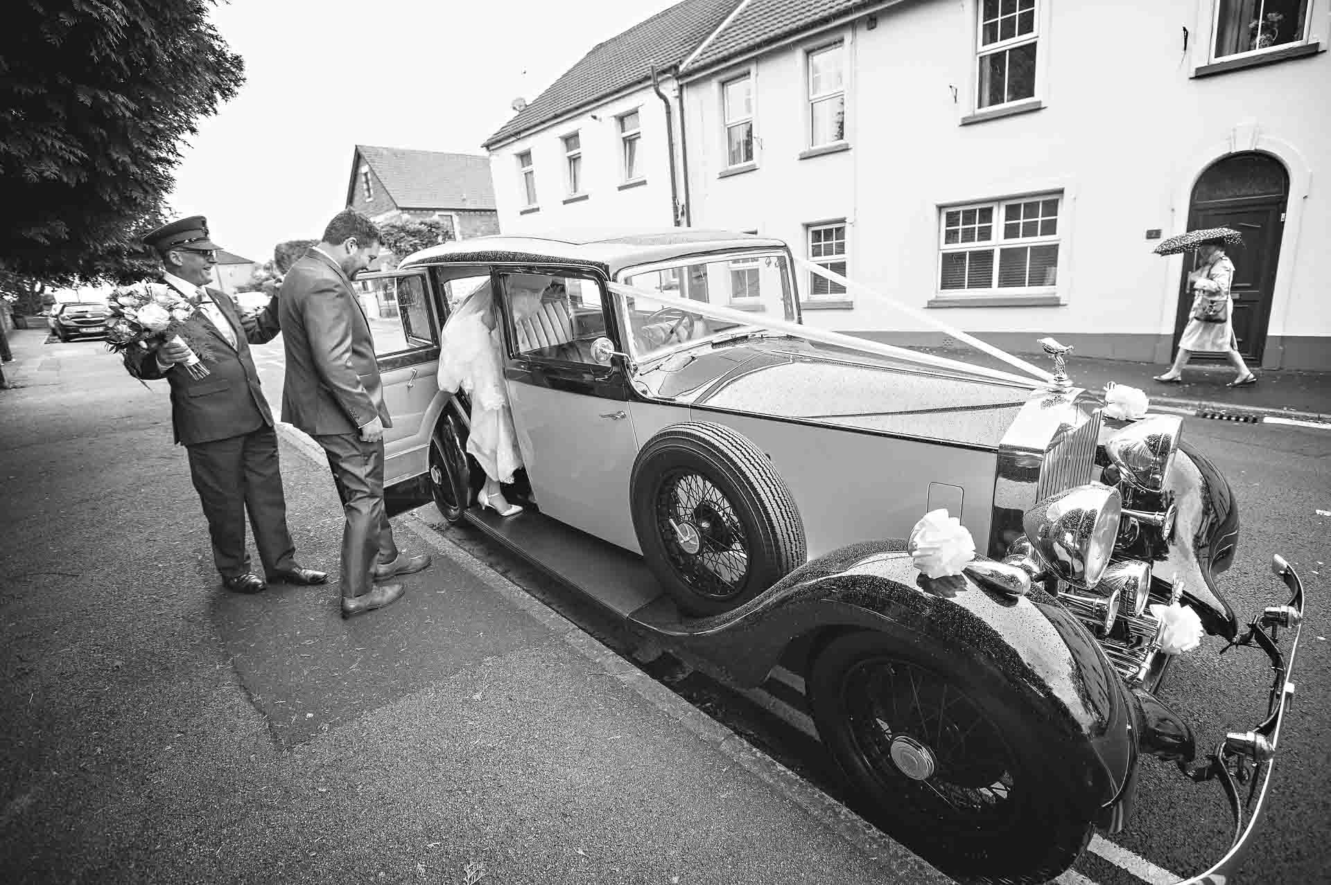 Bride and groom getting into Rolls Royce whilst chauffeur holds bouquet