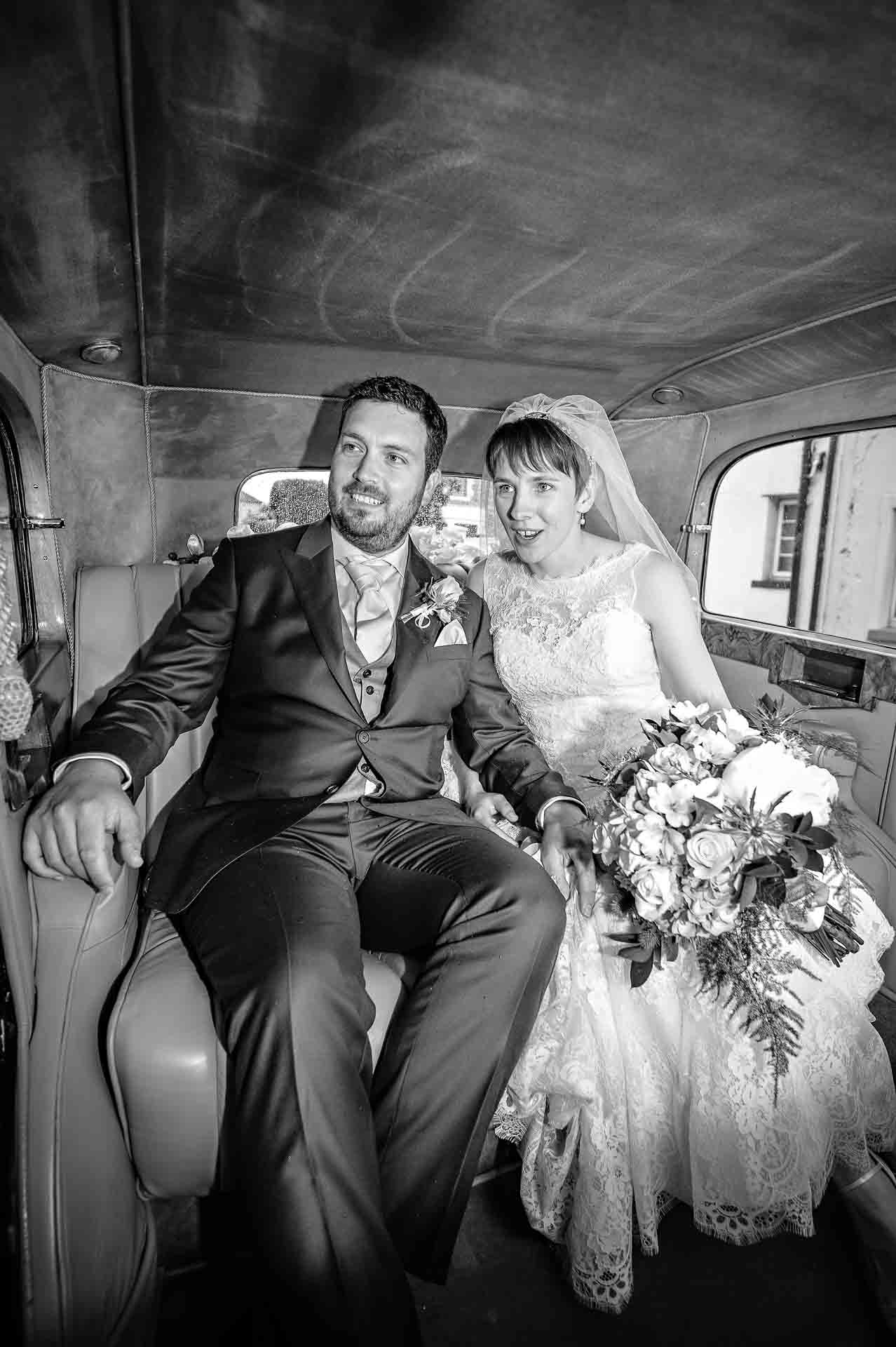 Couple sitting in back of wedding Rolls Royce looking out of window