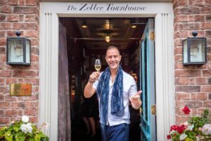 Male wedding guest with blue scarf standing at door to the Zetter Townhouse holding a glass of wine